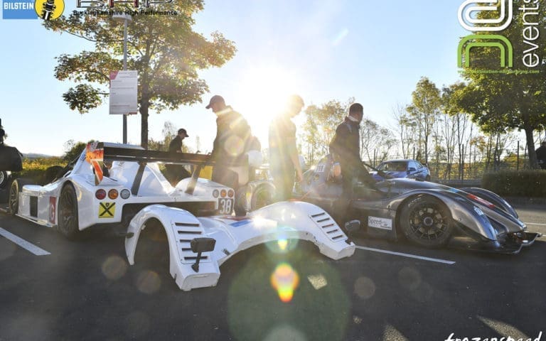 Two Radicals in the car park at the Nurburgring. The sun is shining on them and a burst of light is coming from the sun.