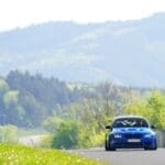 A blue E92 M3 on track with the Eifel mountains and countryside in the background.